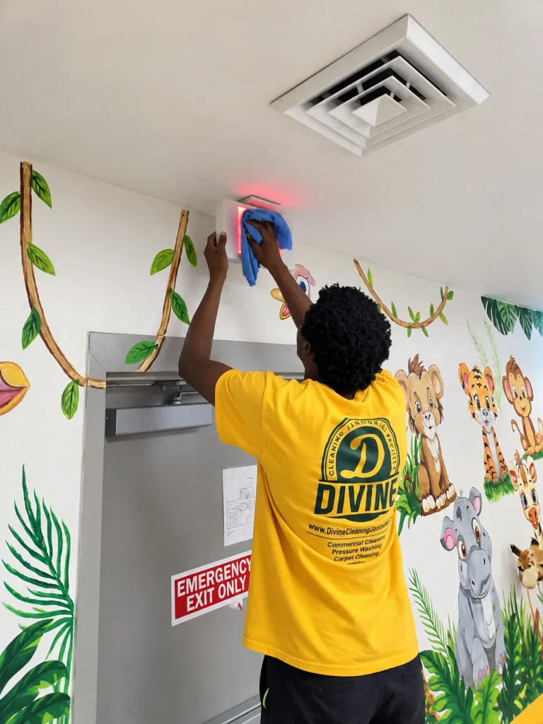 Divine Cleaning and Janitorial team member dusting high surfaces above a door in a daycare classroom