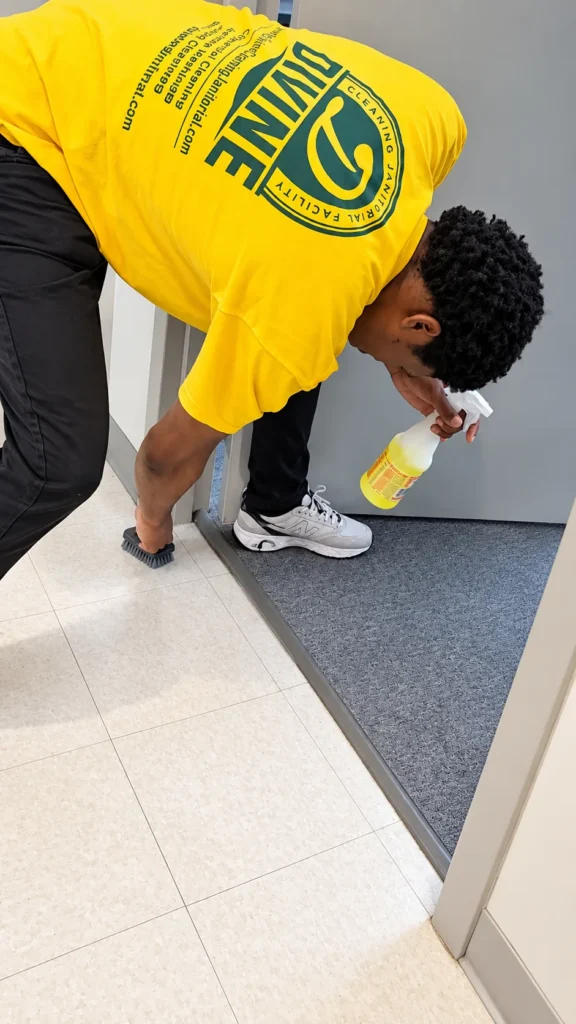Divine Cleaning and Janitorial team member scrubbing a door threshold with a brush and spray cleaner