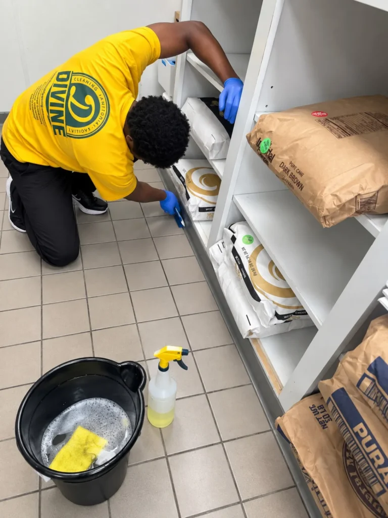 Divine Cleaning and Janitorial team member in gloves wiping down storage shelves with spray cleaner and a bucket